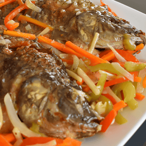 Escabeche is a popular Filipino dish that consists of fried fish or meat, topped with a sweet and sour sauce made from vinegar, soy sauce, sugar, and various spices. This dish has Spanish origins and the name "escabeche" comes from the Spanish word "escabechar", which means to marinate in an acidic solution.